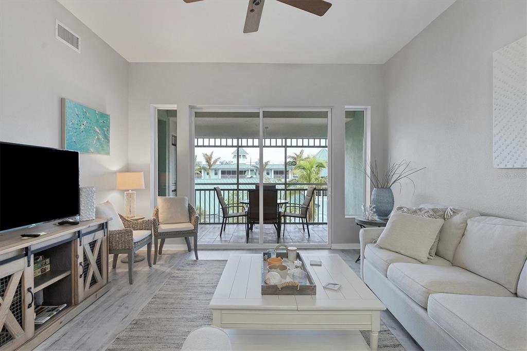 A living room features a white sofa, coffee table, and sliding doors opening to a balcony — 5117 MELBOURNE STREET UNIT B4302, PORT CHARLOTTE, FL