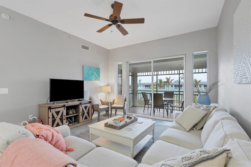 A living room features a white sofa, coffee table, television console, and a sliding glass door — 5117 MELBOURNE STREET UNIT B4302, PORT CHARLOTTE, FL