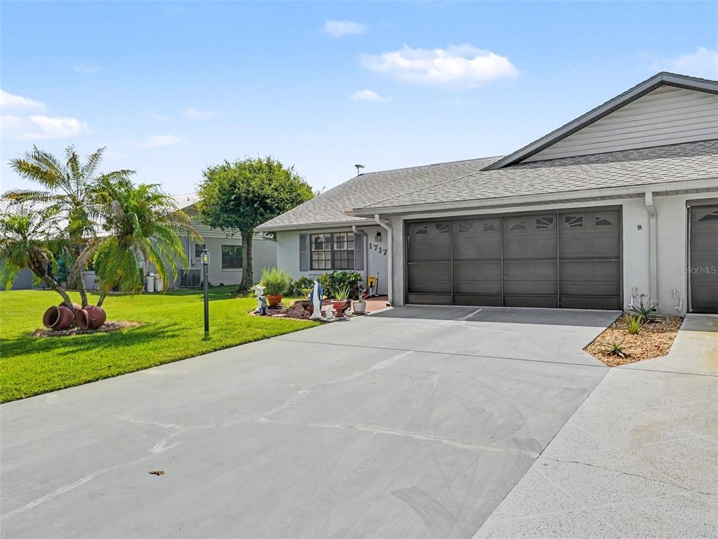 A single-story house features a gray garage door, a concrete driveway, and a palm tree — 1717 W ORANGEWOOD LANE UNIT 4, AVON PARK, FL