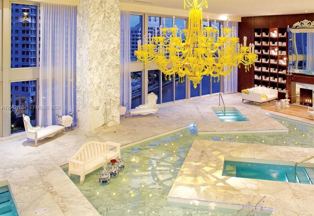 A luxurious indoor pool room features a large yellow chandelier, marble flooring, and floor-to-ceiling windows — 495 Brickell Ave # 4609, Miami FL 33131, MIAMI, FL