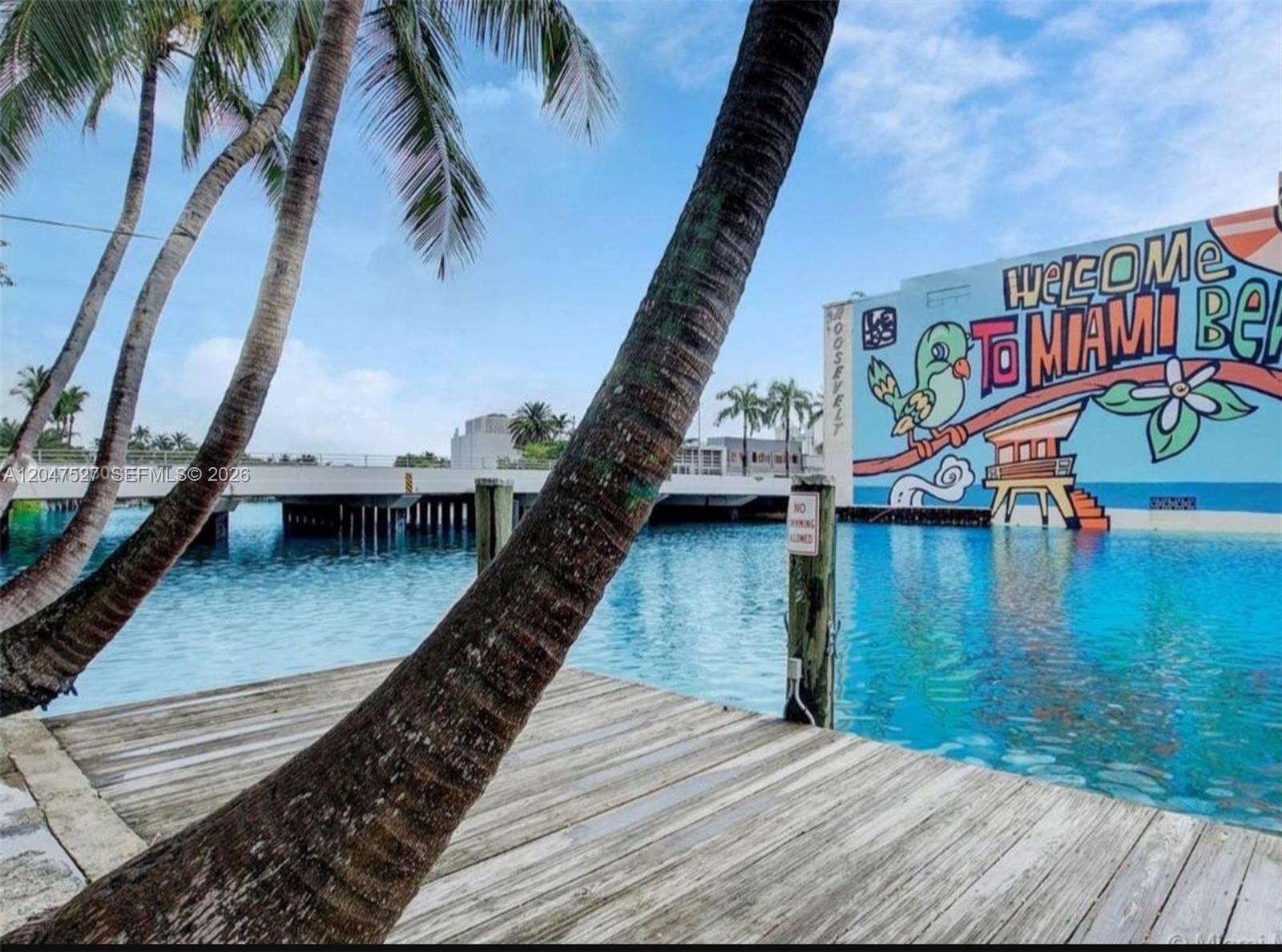 A wooden dock sits on the water in front of a mural-covered building and bridge — 4035 N Meridian Ave PH, Miami Beach FL 33140, MIAMI BEACH, FL