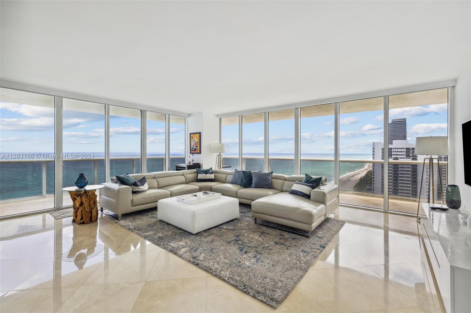 A modern living room features a large sectional sofa, floor-to-ceiling windows, and ocean views — 1830 S OCEAN DR # 2102, Hallandale Beach FL 33009, HALLANDALE BEACH, FL