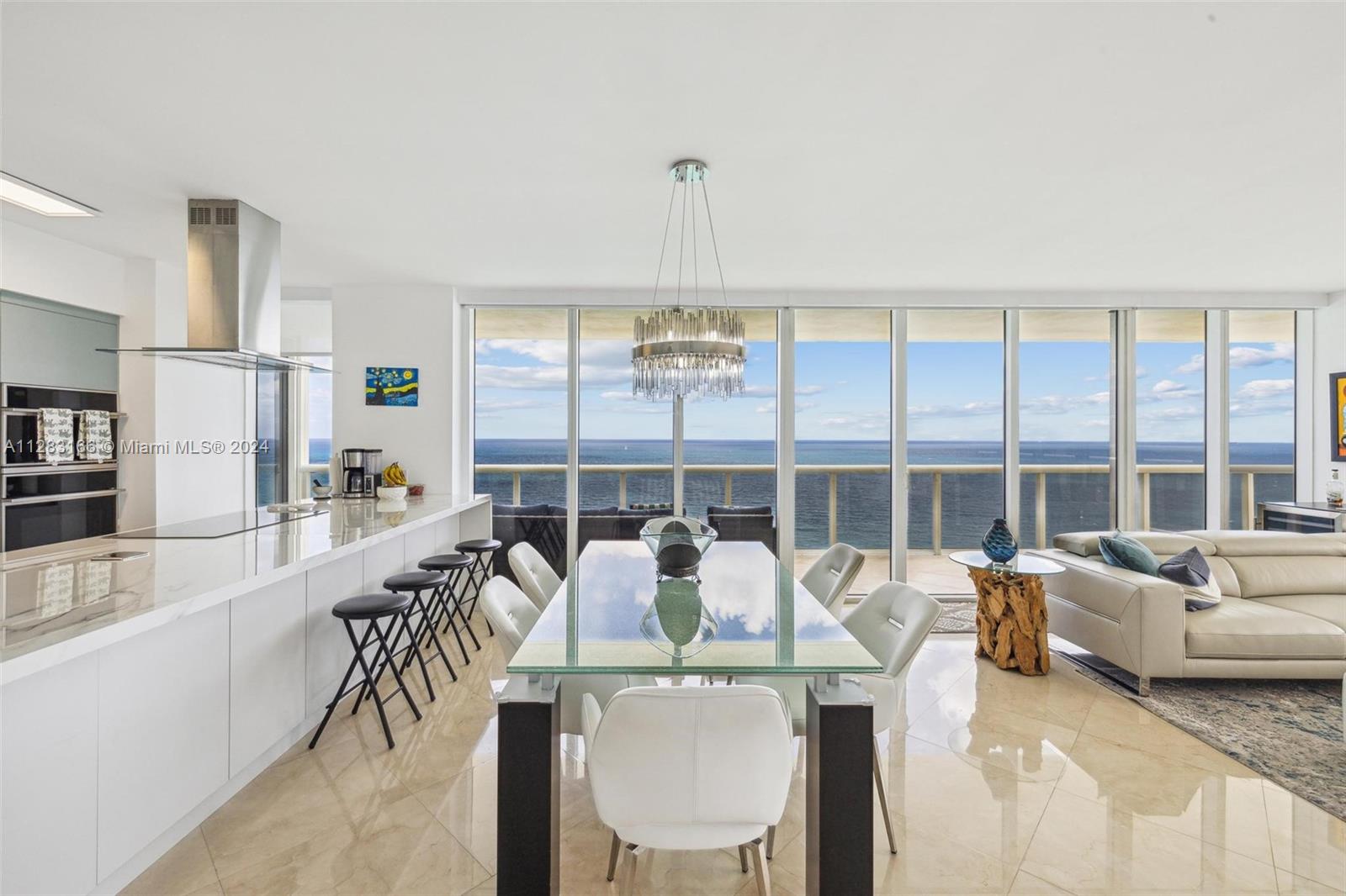 A modern dining area and kitchen feature a glass table, white chairs, and ocean views — 1830 S OCEAN DR # 2102, Hallandale Beach FL 33009, HALLANDALE BEACH, FL