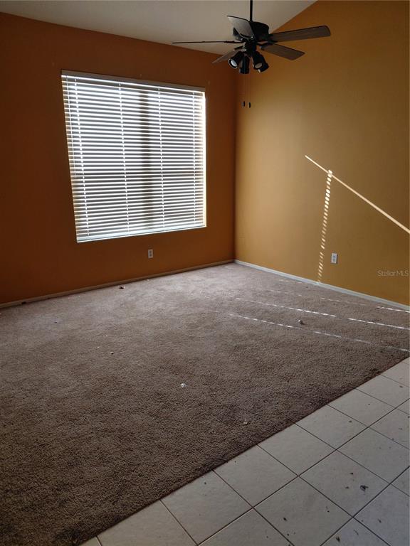 An empty room with tan walls, brown carpet, a ceiling fan, and a large window — 18124 ANTIETAM COURT, TAMPA, FL