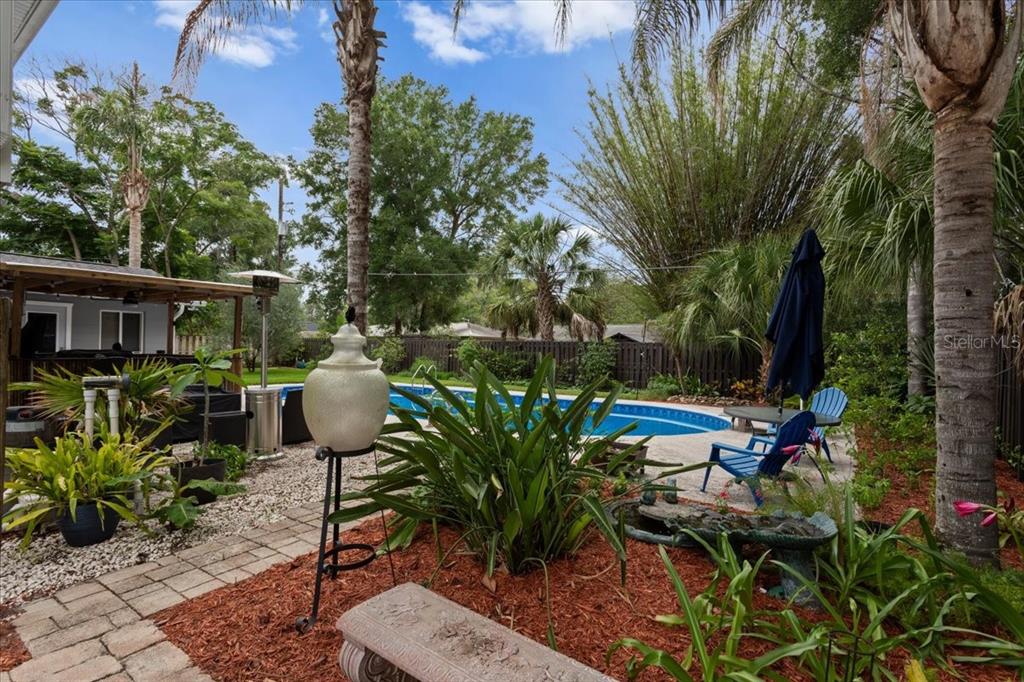 A backyard features a swimming pool, patio furniture, palm trees, and a stone bench — 1940 NW 35TH STREET, GAINESVILLE, FL
