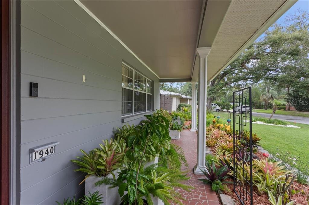 A covered front porch features gray siding, a tiled floor, and lush landscaping — 1940 NW 35TH STREET, GAINESVILLE, FL