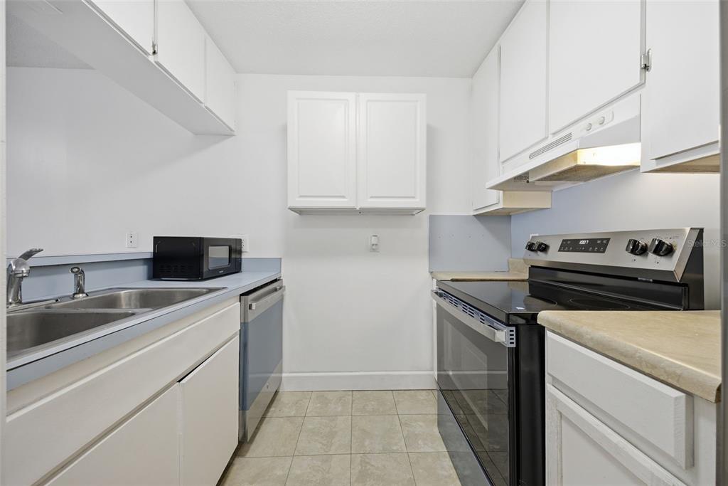 A galley kitchen features white cabinets, light countertops, a black stove, and a double sink — 141 FERNERY ROAD UNIT A3, LAKELAND, FL