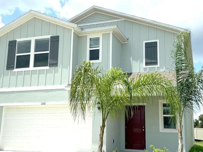 A two-story house with light green vertical siding, a white garage door, and palm trees — 11921 NOBLE CHASE PATH, DADE CITY, FL