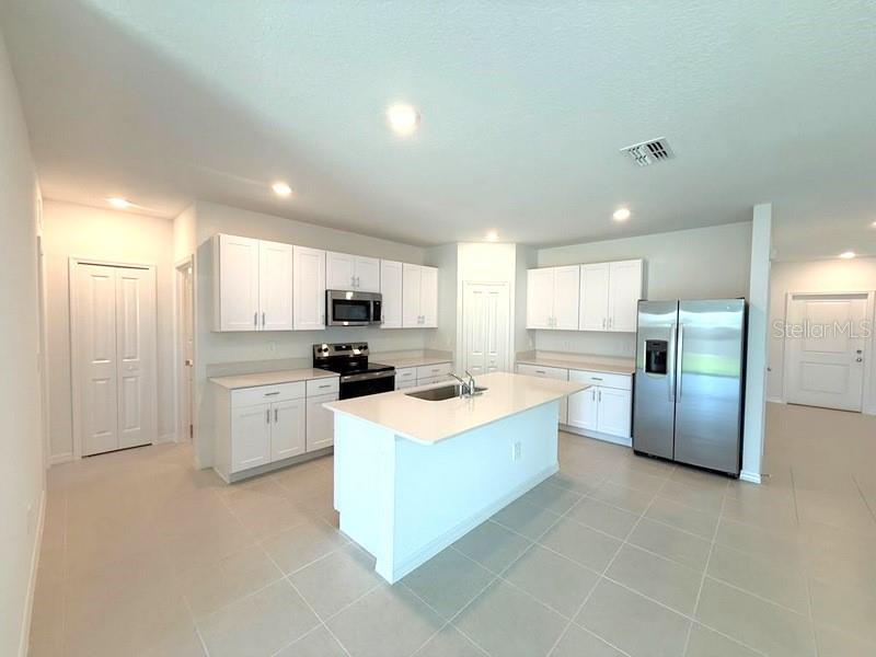 A kitchen features white cabinets, a central island, stainless steel appliances, and light tile flooring — 11921 NOBLE CHASE PATH, DADE CITY, FL