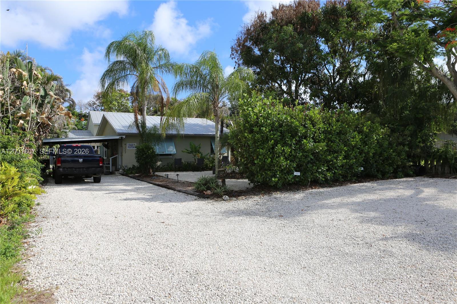 A one-story house with a metal roof and gravel driveway sits behind lush landscaping — 4225 SE Westfield St, Stuart FL 34997, STUART, FL