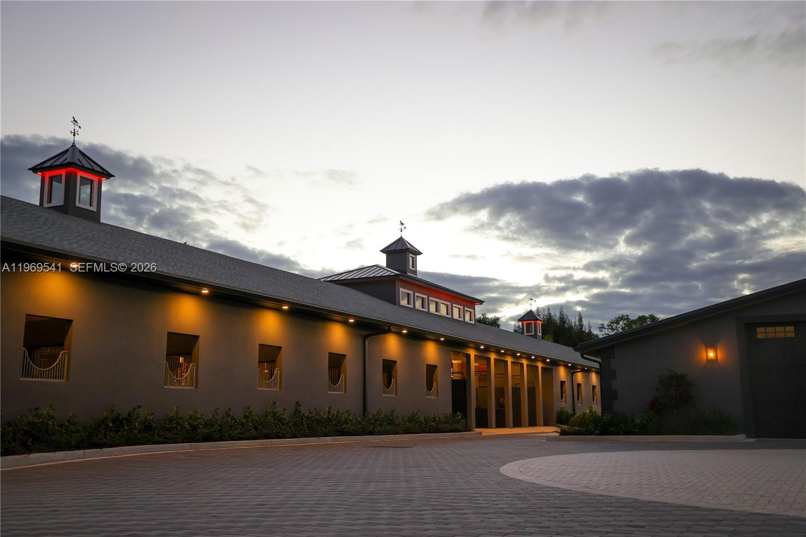 An exterior view of a modern stable building with cupolas and paved driveway at dusk — 2625 SW 148th Ave, Davie FL 33331, DAVIE, FL