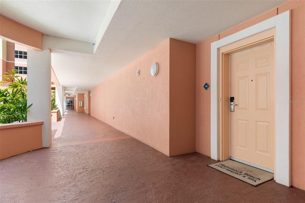 An outdoor hallway with peach-colored walls leads to a door with a resort doormat — 200 OCEAN CREST DRIVE UNIT 108, PALM COAST, FL