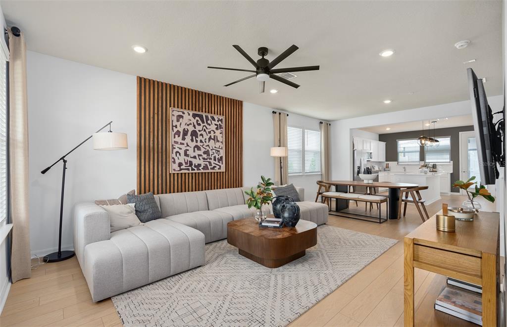 A living room with a sectional sofa, wood-slat accent wall, and an open-concept dining area — 6355 ARGENT WOOD DRIVE, WINTER GARDEN, FL