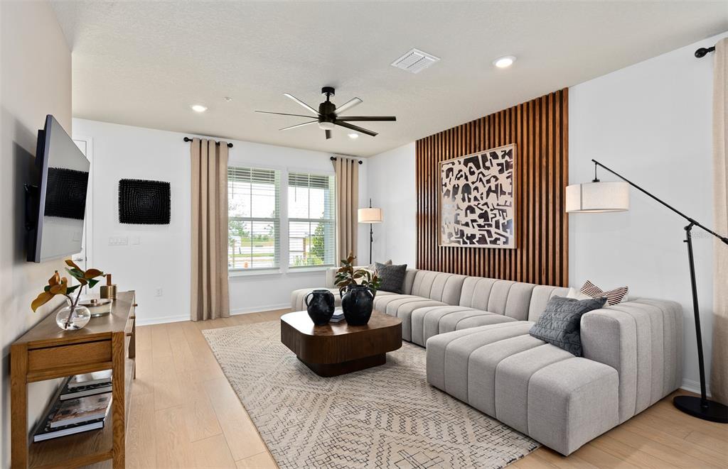 A living room features a light gray sectional sofa, wood-slat accent wall, and wood flooring — 6355 ARGENT WOOD DRIVE, WINTER GARDEN, FL