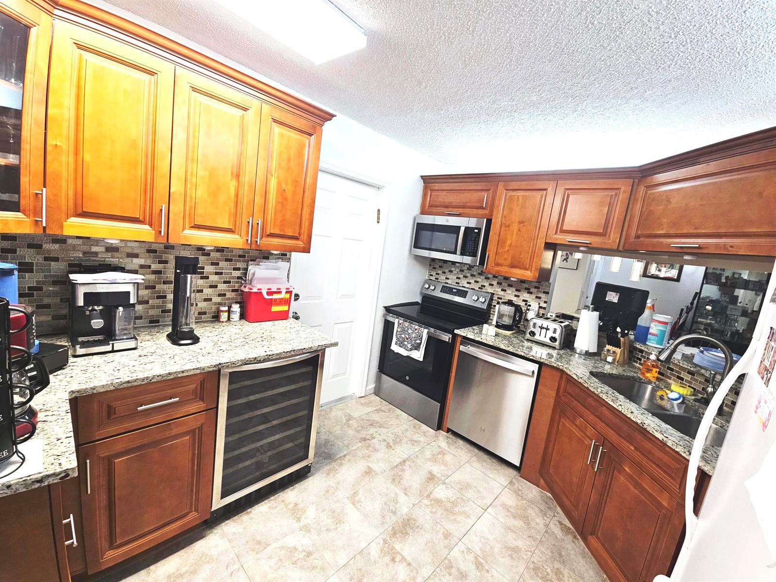A kitchen features wood cabinets, granite countertops, stainless steel appliances, and a wine refrigerator — 16 Vía De Casas Sur # 103, Boynton Beach FL 33426, BOYNTON BEACH, FL