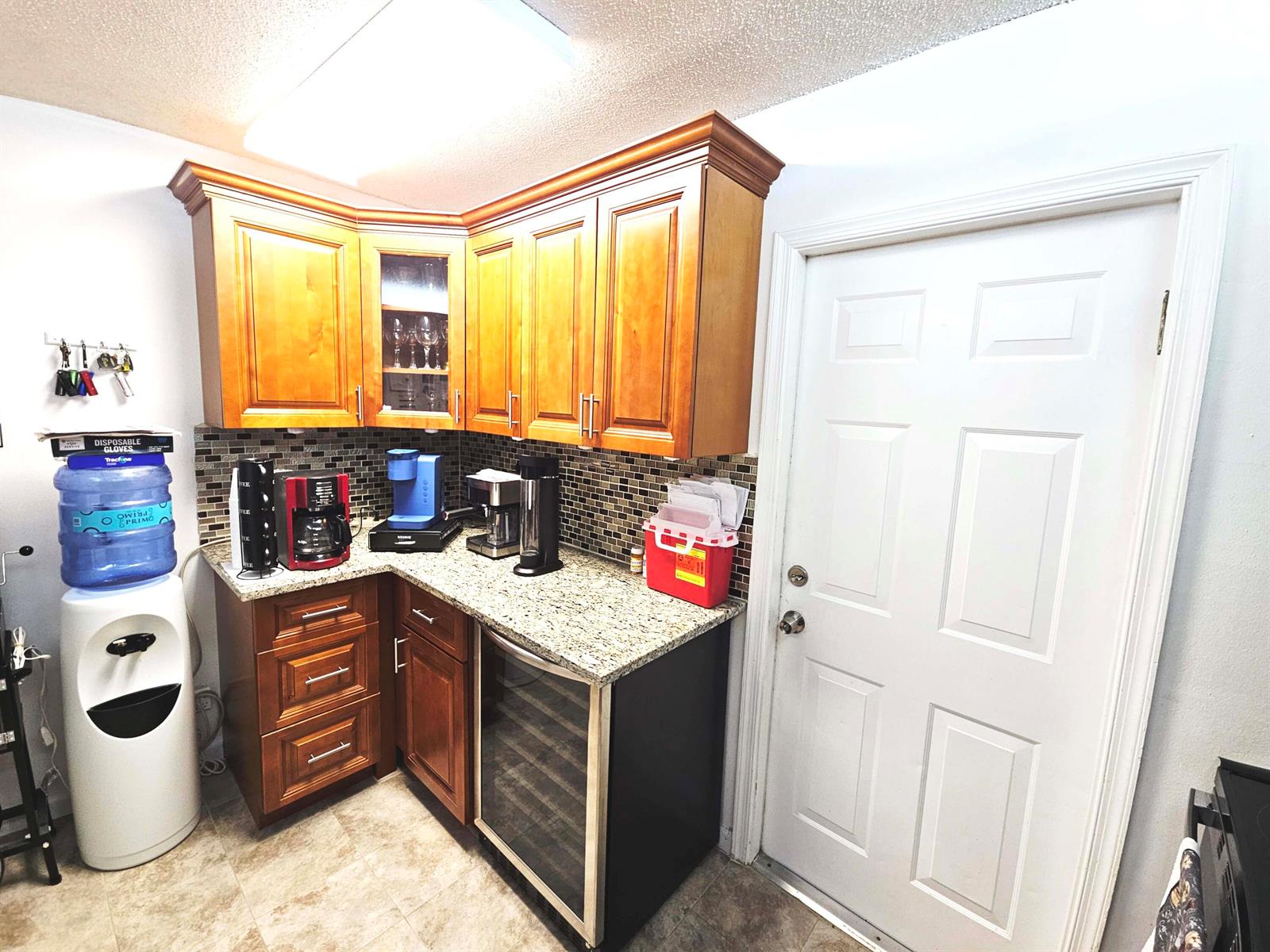 A kitchen corner features wood cabinets, granite countertops, a wine cooler, and a water dispenser — 16 Vía De Casas Sur # 103, Boynton Beach FL 33426, BOYNTON BEACH, FL