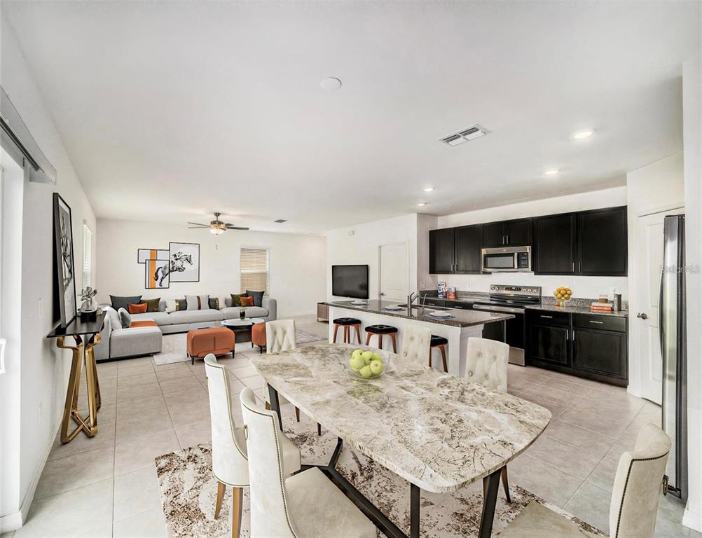 An open-concept kitchen and dining area features dark cabinets, granite countertops, and tile flooring — 2871 SILVER SCALLOP LOOP, WIMAUMA, FL