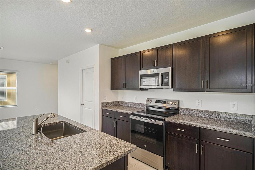 A kitchen features dark wood cabinets, granite countertops, stainless steel appliances, and a central island — 2871 SILVER SCALLOP LOOP, WIMAUMA, FL