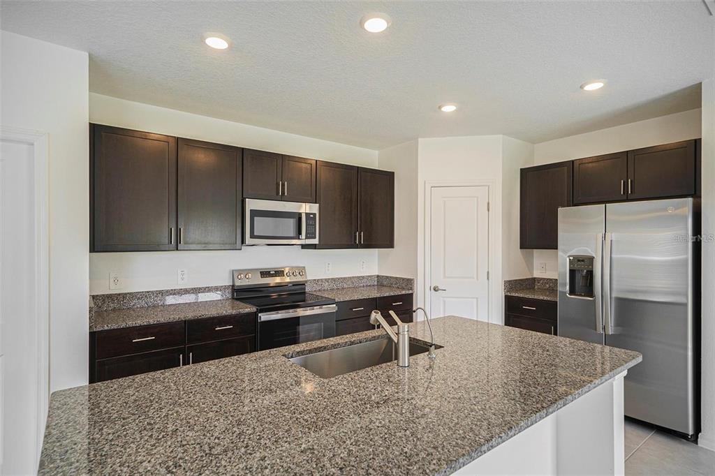 A kitchen features dark wood cabinets, granite countertops, stainless steel appliances, and a central island — 2871 SILVER SCALLOP LOOP, WIMAUMA, FL