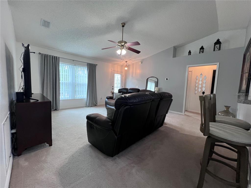 A living room features a dark leather sofa, carpeted floors, and a vaulted ceiling — 632 N GOODRICH DRIVE, DELTONA, FL