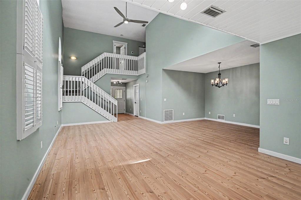 A spacious living area features light wood flooring, a white staircase, and high vaulted ceilings — 34 BRISTOL DRIVE, PALM COAST, FL