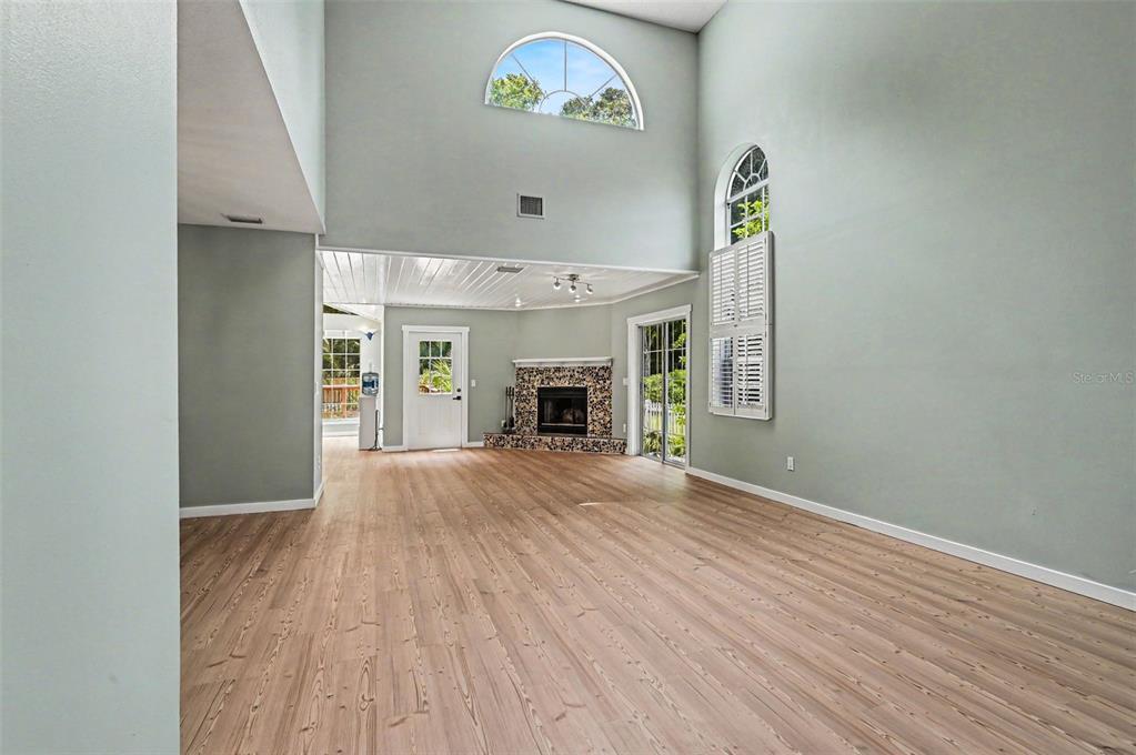 A high-ceilinged living room features light wood flooring, a tiled fireplace, and large windows — 34 BRISTOL DRIVE, PALM COAST, FL