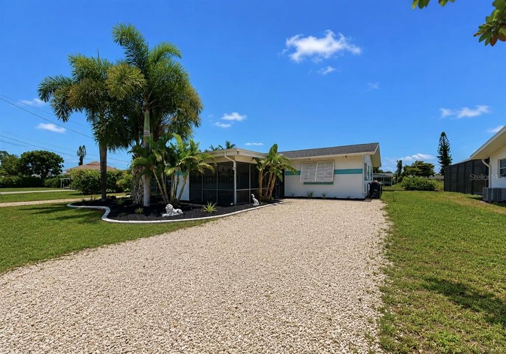 A single-story house with a gravel driveway, screened porch, and palm trees under a blue sky — 4933 VICTORIA DRIVE, CAPE CORAL, FL