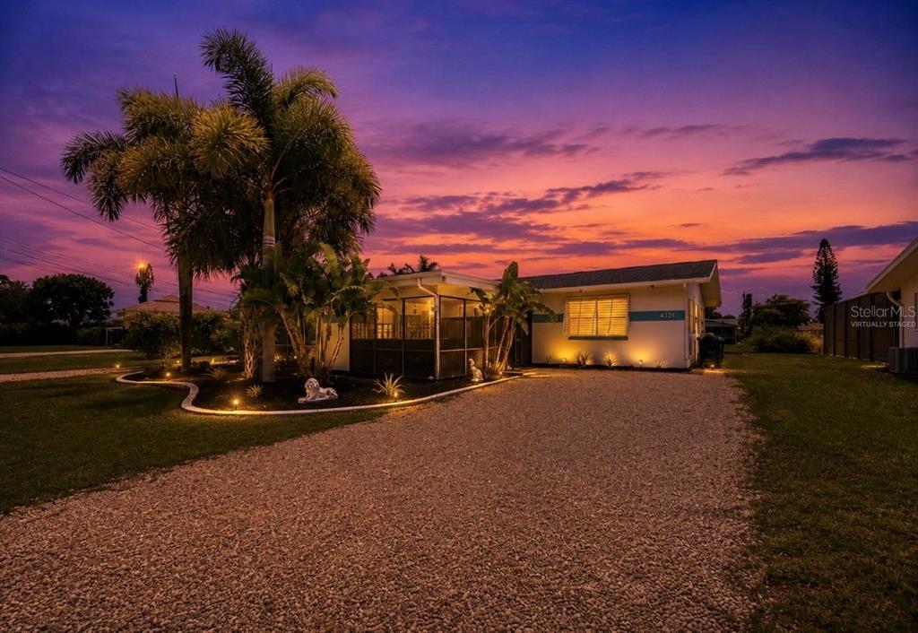 A single-story house with a gravel driveway and a screened porch at sunset — 4933 VICTORIA DRIVE, CAPE CORAL, FL