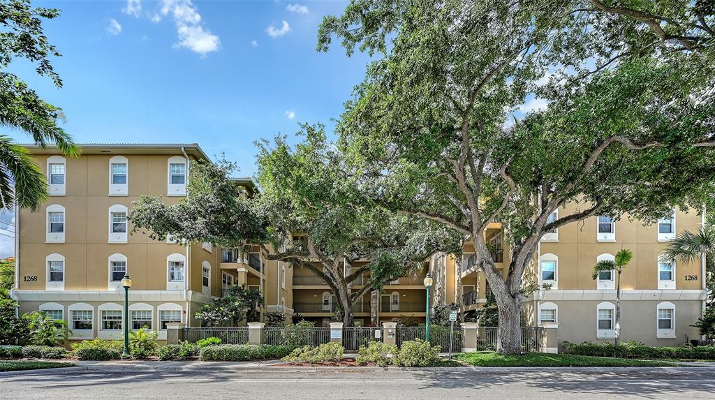 A multi-story tan apartment building is partially obscured by large, mature trees — 1268 11TH STREET UNIT 2404, SARASOTA, FL