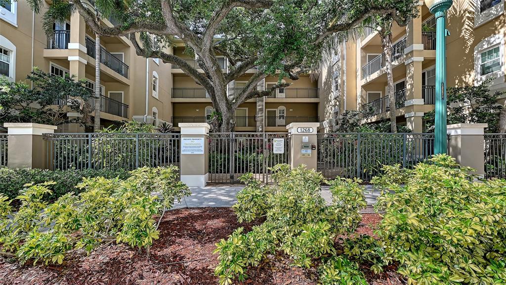 A gated entrance to a multi-story apartment building features a large tree and landscaping — 1268 11TH STREET UNIT 2404, SARASOTA, FL