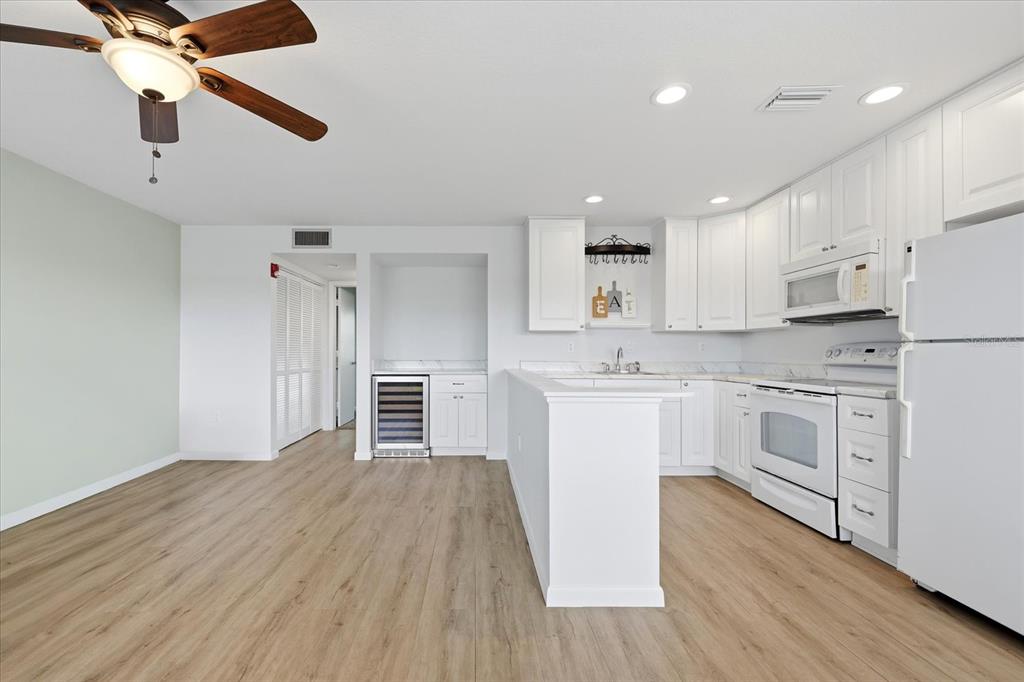 A kitchen with white cabinets, light wood flooring, and a wine cooler in an open room — 1001 77TH AVENUE N UNIT 307, ST PETERSBURG, FL