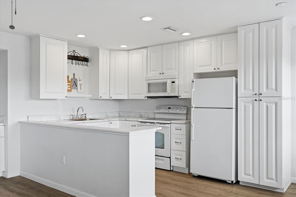 A kitchen with white cabinets, white appliances, and a peninsula counter with a sink — 1001 77TH AVENUE N UNIT 307, ST PETERSBURG, FL