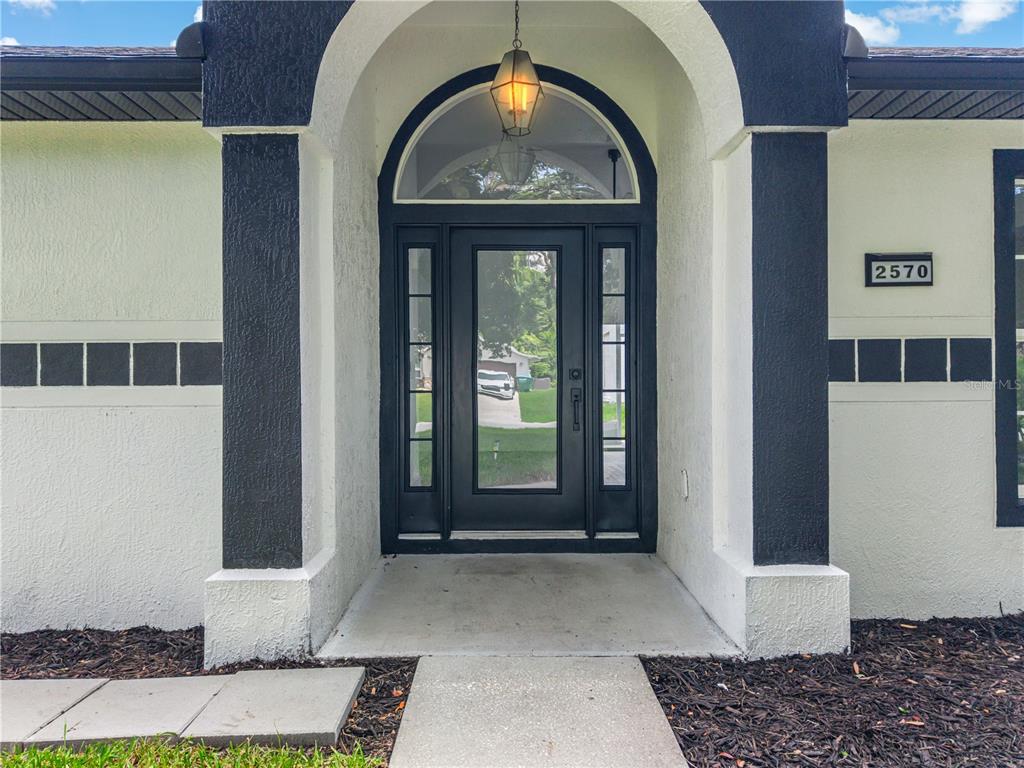 The front entrance features a black-framed glass door with sidelights and an arched transom window — 2570 COACHMAN DRIVE, DELTONA, FL