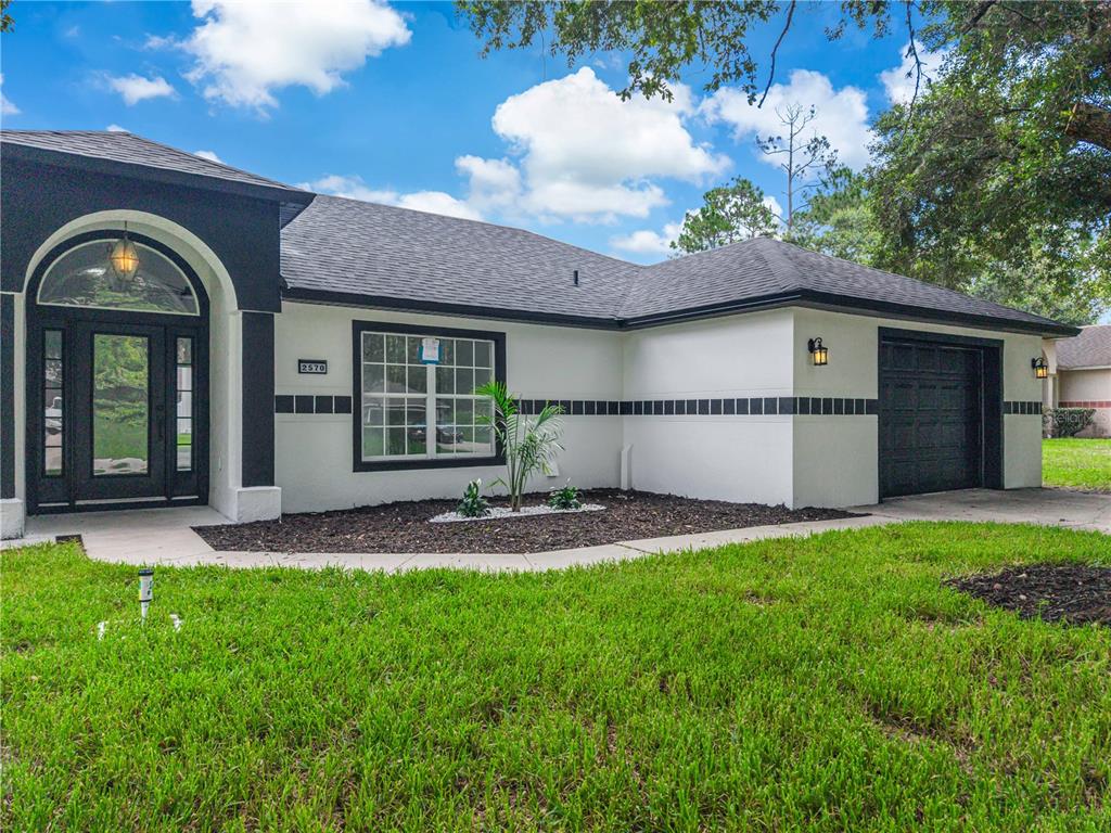 A single-story house with white stucco walls, black trim, and a black garage door — 2570 COACHMAN DRIVE, DELTONA, FL