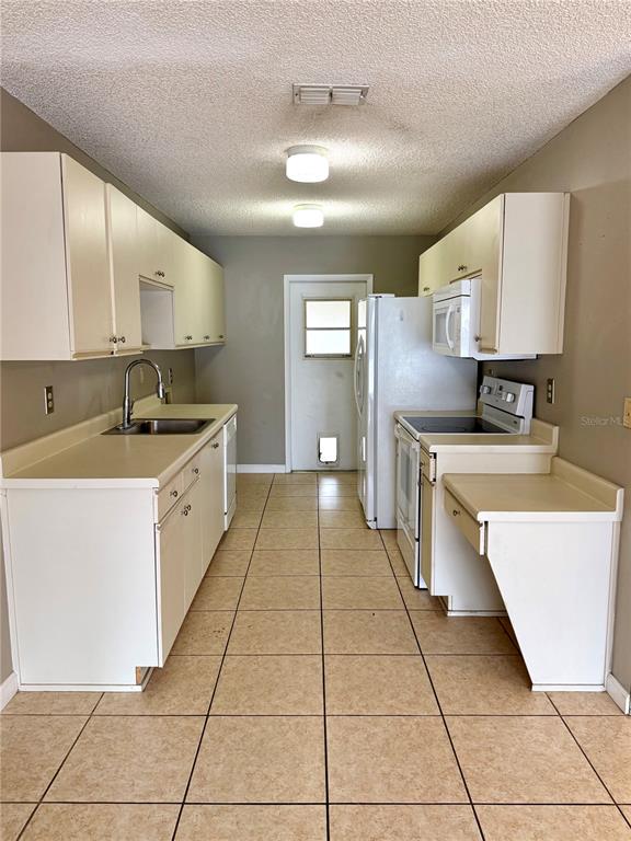 A galley kitchen features white cabinets, beige tile flooring, and a white refrigerator — 242 WINTER RIDGE BOULEVARD UNIT 242, WINTER HAVEN, FL