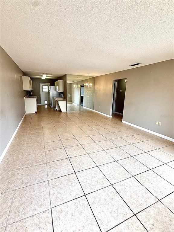 A spacious room with light-colored tile flooring, a kitchen area, and a mirrored wall — 242 WINTER RIDGE BOULEVARD UNIT 242, WINTER HAVEN, FL
