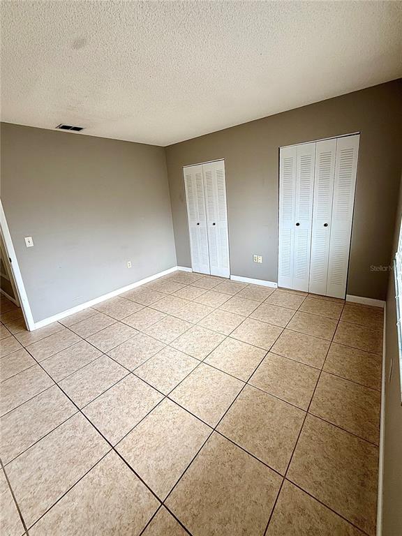 A bedroom with beige walls, tiled flooring, and two sets of white louvered closet doors — 242 WINTER RIDGE BOULEVARD UNIT 242, WINTER HAVEN, FL