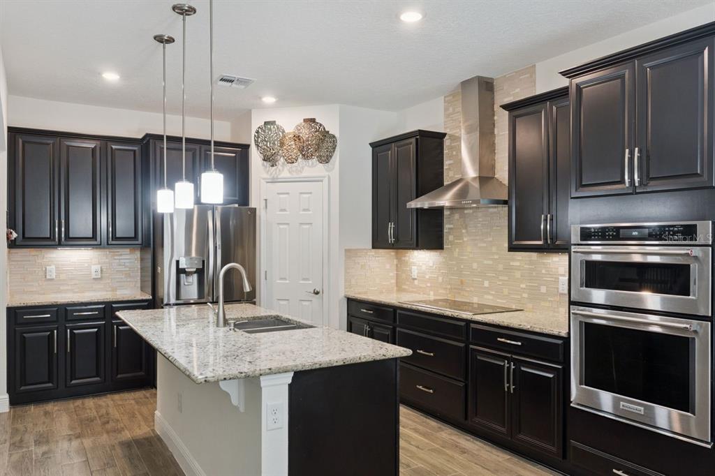 A kitchen features dark wood cabinets, granite countertops, stainless steel appliances, and a central island — 3169 PINENUT DRIVE, APOPKA, FL