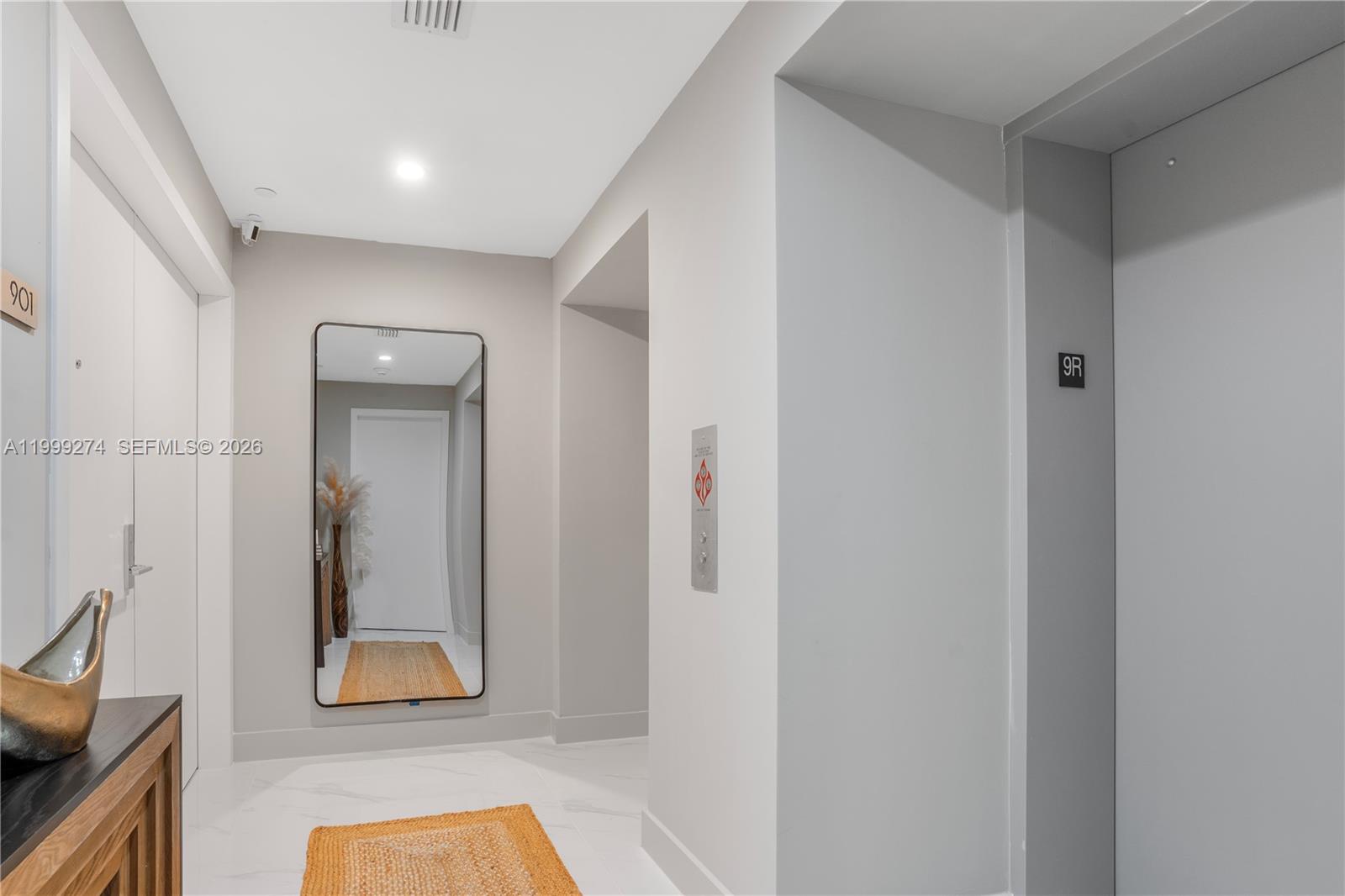 A modern hallway features a large wall mirror, white tile flooring, and an elevator entrance — 700 NE 24 # 901, Miami FL 33137, MIAMI, FL