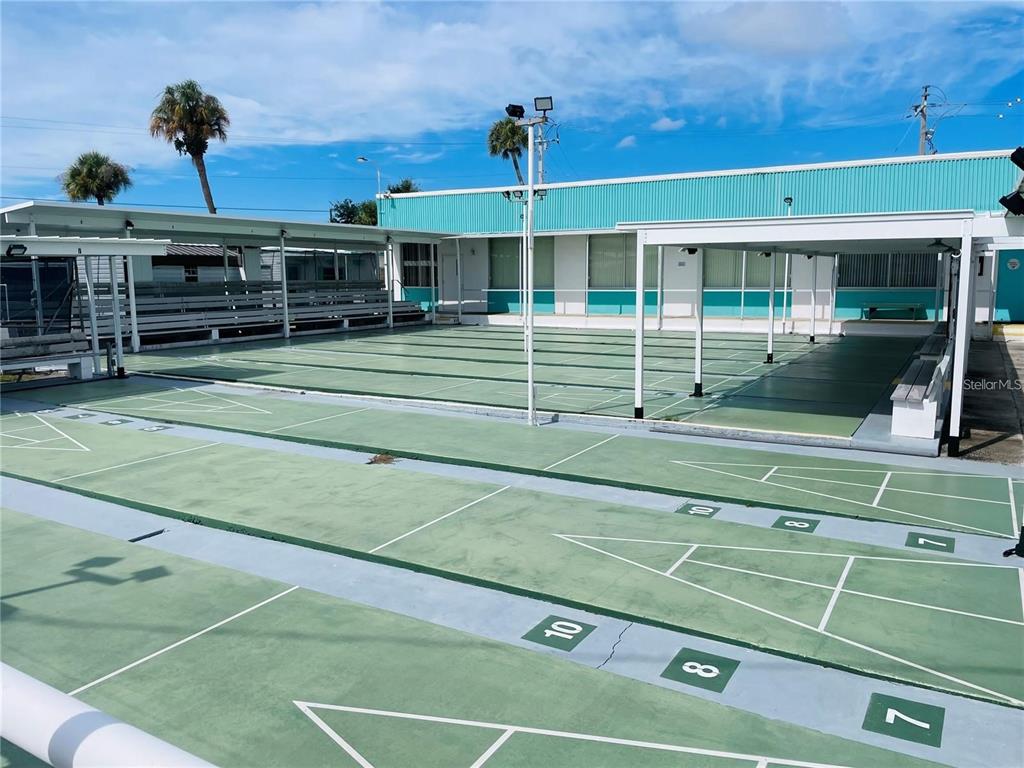 An outdoor shuffleboard court with painted markings sits in front of a teal building — 21 ILLINOIS STREET, PALMETTO, FL