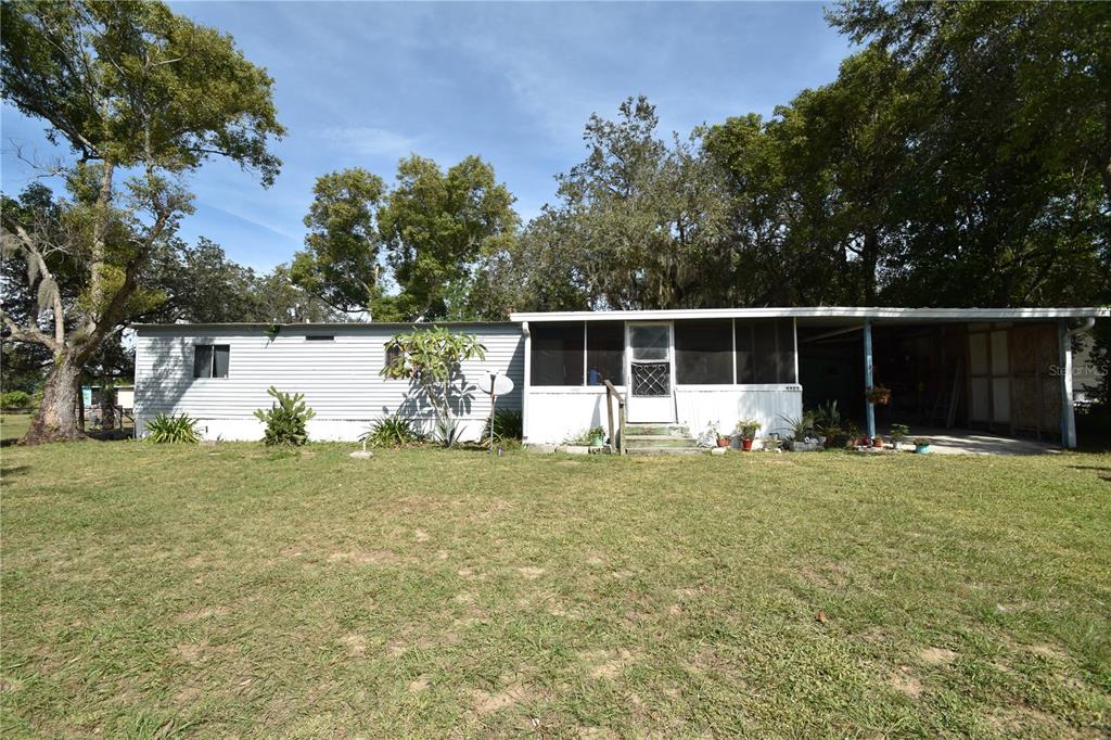 A single-story mobile home with a screened-in porch and an attached carport sits on grass — 5722 LITTLE EVA ROAD, HAINES CITY, FL
