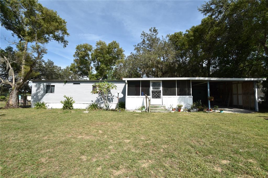 A single-story mobile home with a screened-in porch and an attached carport sits on grass — 5722 LITTLE EVA ROAD, HAINES CITY, FL