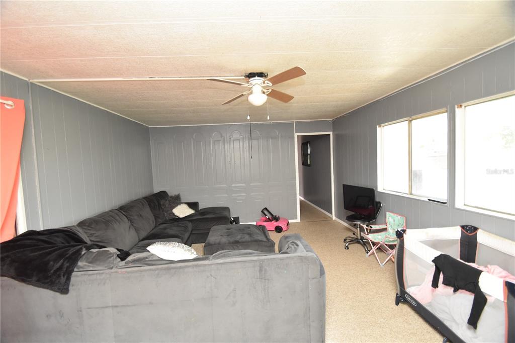 A living room features gray paneled walls, a ceiling fan, a sectional sofa, and windows — 5722 LITTLE EVA ROAD, HAINES CITY, FL