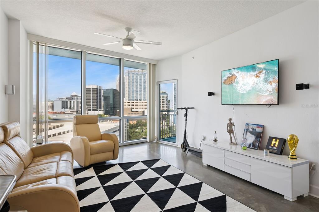 A modern living room features a leather sofa, patterned rug, and floor-to-ceiling windows with city views — 322 E CENTRAL BOULEVARD UNIT 1107, ORLANDO, FL