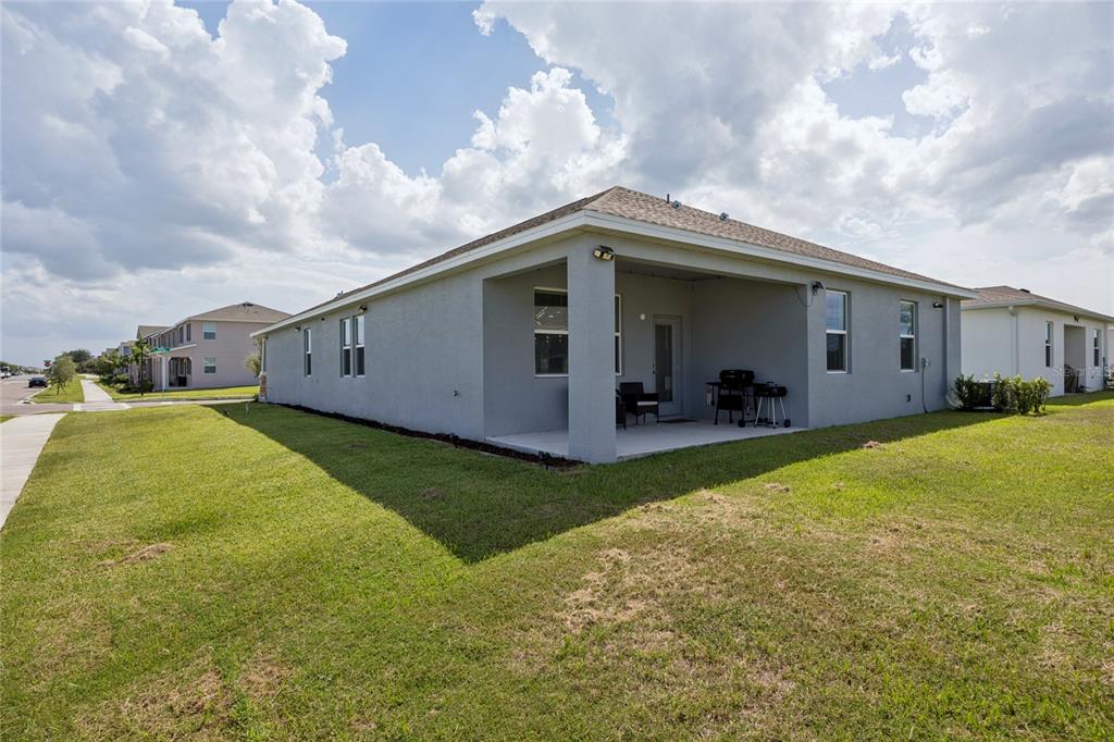 The exterior of a gray stucco house features a covered patio and a grassy yard — 2466 RELAXING LANE, KISSIMMEE, FL