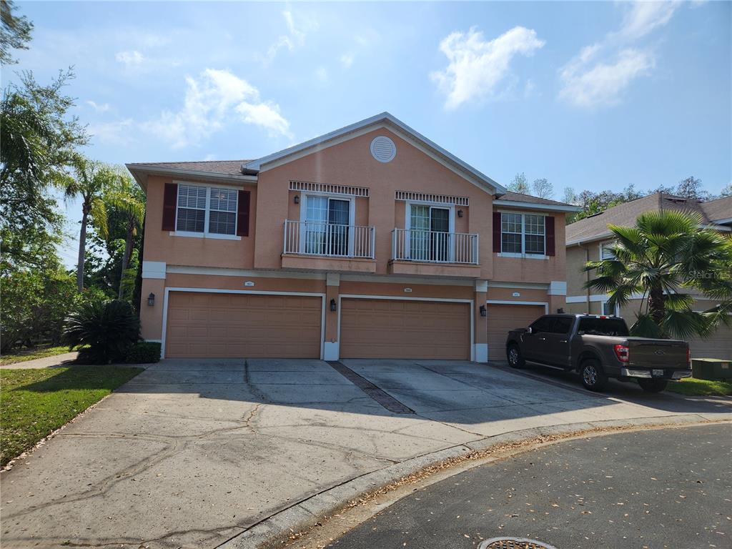 A two-story townhouse exterior features three garage doors, two balconies, and a concrete driveway — 8612 GREAT EGRET TRACE, NEW PORT RICHEY, FL