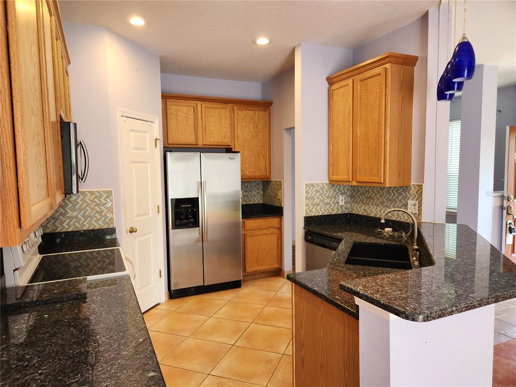 A kitchen with oak cabinets, dark granite countertops, stainless steel appliances, and a tile floor — 8612 GREAT EGRET TRACE, NEW PORT RICHEY, FL