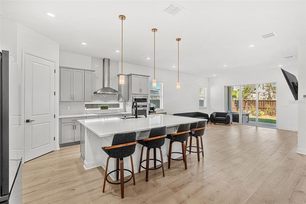A modern kitchen features a large white island with four stools and grey cabinetry — 3085 EXPEDITION DRIVE, ST CLOUD, FL