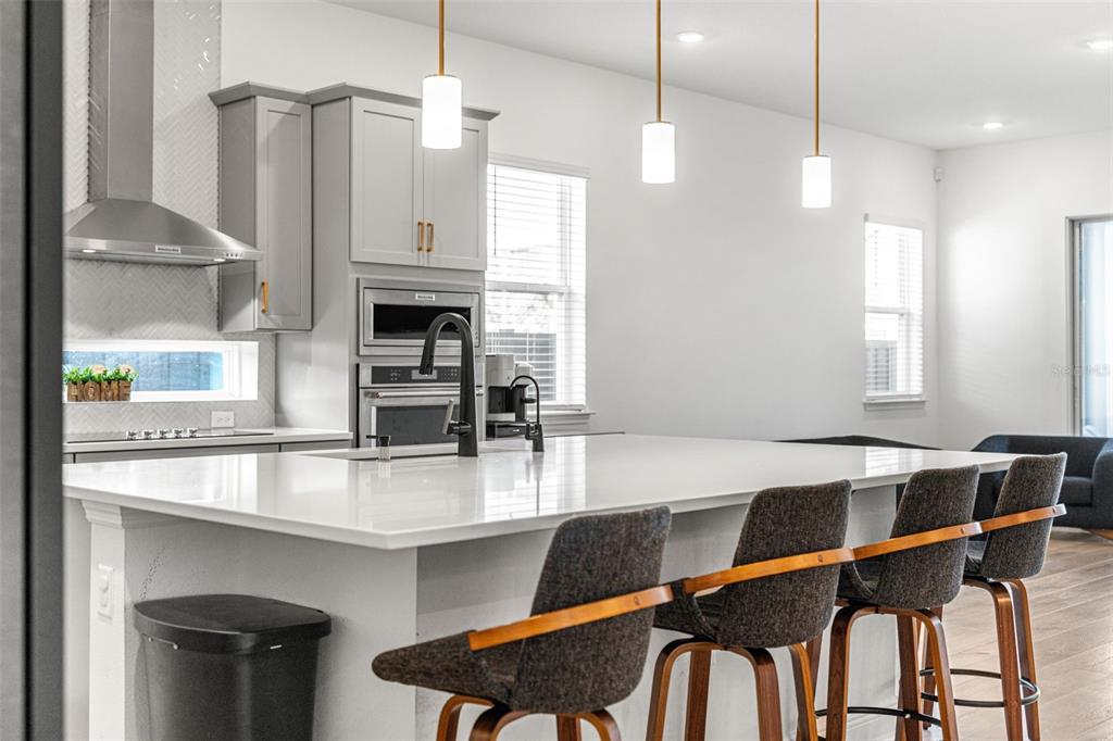 A modern kitchen features a large white island, gray cabinetry, and three hanging pendant lights — 3085 EXPEDITION DRIVE, ST CLOUD, FL