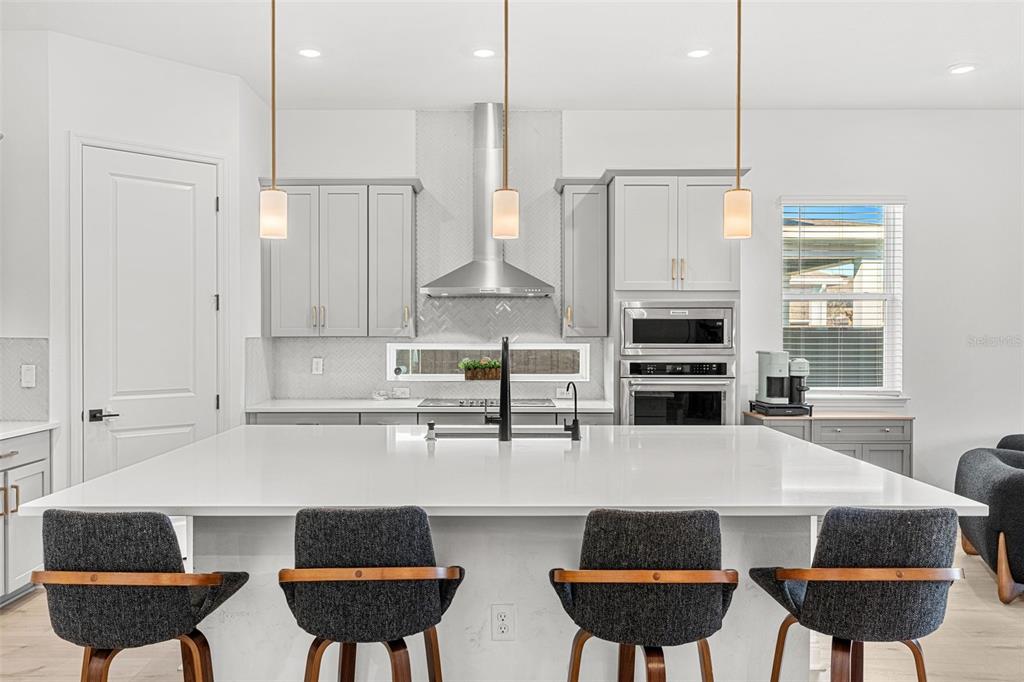 A modern kitchen features a large white island, gray cabinets, and three hanging pendant lights — 3085 EXPEDITION DRIVE, ST CLOUD, FL